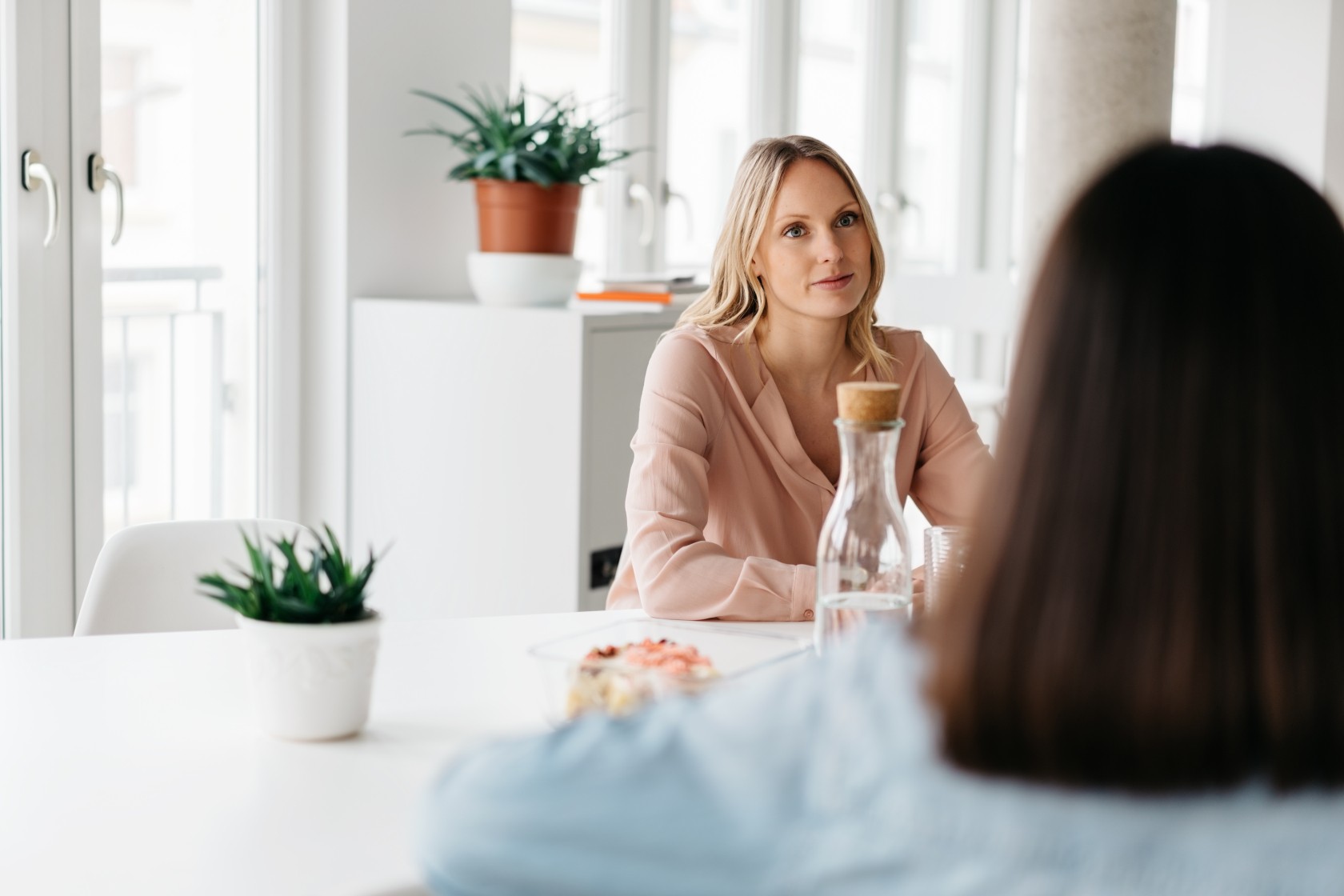 Two office colleagues having a meeting or discussion over refreshments at a cafeteria or canteen in an over the shoulder view of an attentive young woman listening